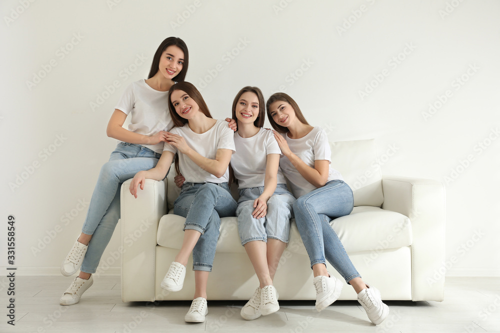 Beautiful young ladies in jeans and white t-shirts on sofa indoors. Woman's Day Beautiful young ladies in jeans and white t-shirts on sofa indoors. Woman's Day