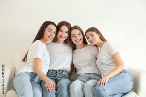 Beautiful young ladies in jeans and white t-shirts on sofa indoors. Woman's Day © New Africa