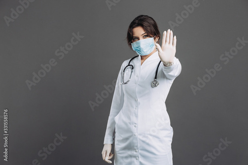 Female doctor with stethoscope wearing mask and glasses shows stop coronavirus. Covid-19 concept