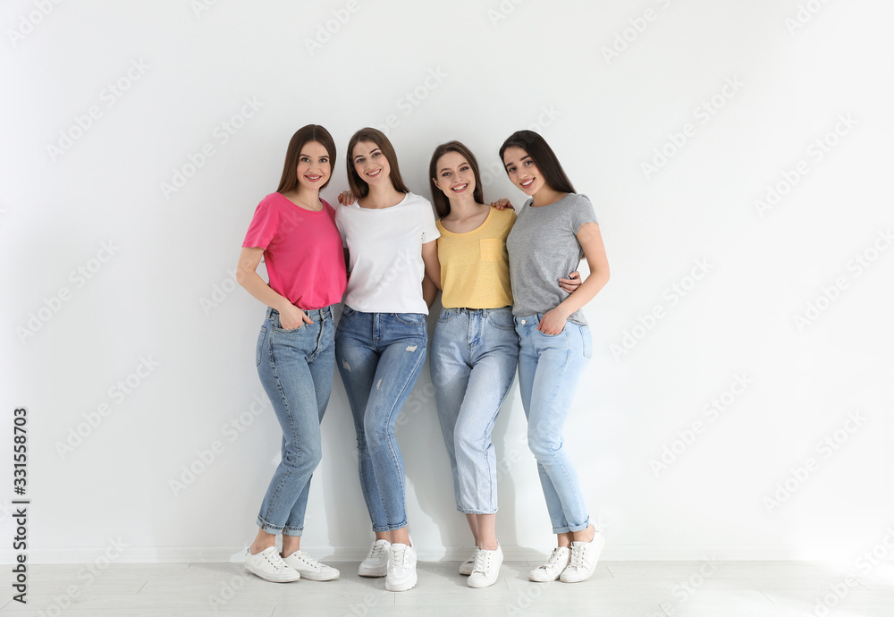 Beautiful young ladies in jeans and colorful t-shirts near white wall indoors. Woman's Day