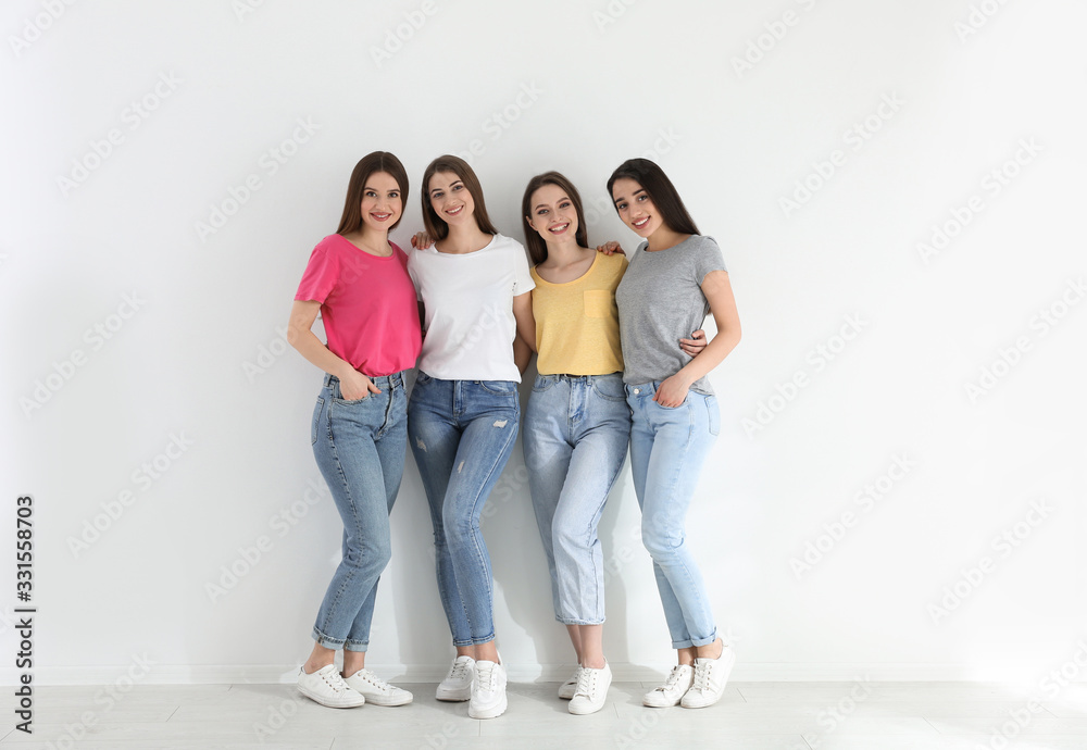 Beautiful young ladies in jeans and colorful t-shirts near white wall indoors. Woman's Day Beautiful young ladies in jeans and colorful t-shirts near white wall indoors. Woman's Day