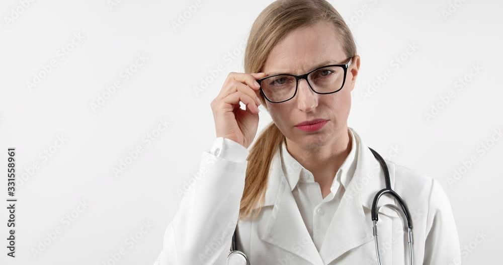 Beautiful middle-aged woman in medical uniform and eyeglasses looking at camera over white background. Female doctor with stethoscope on neck posing in studio. Beautiful middle-aged woman in medical uniform and eyeglasses looking at camera over white background. Female doctor with stethoscope on neck posing in studio.