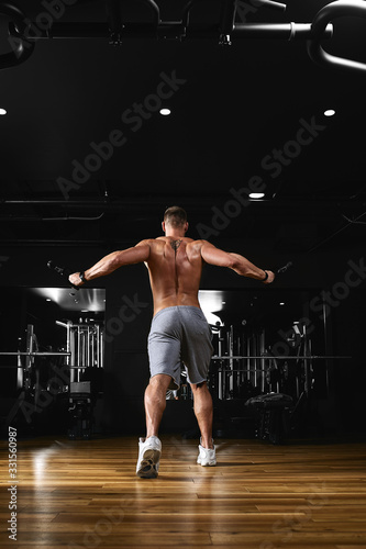 A man trains his arms and chest in the gym on the simulator, does exercises for different muscle groups. Fintes motivation, sports lifestyle, health, athletic body, body positive. Film grain