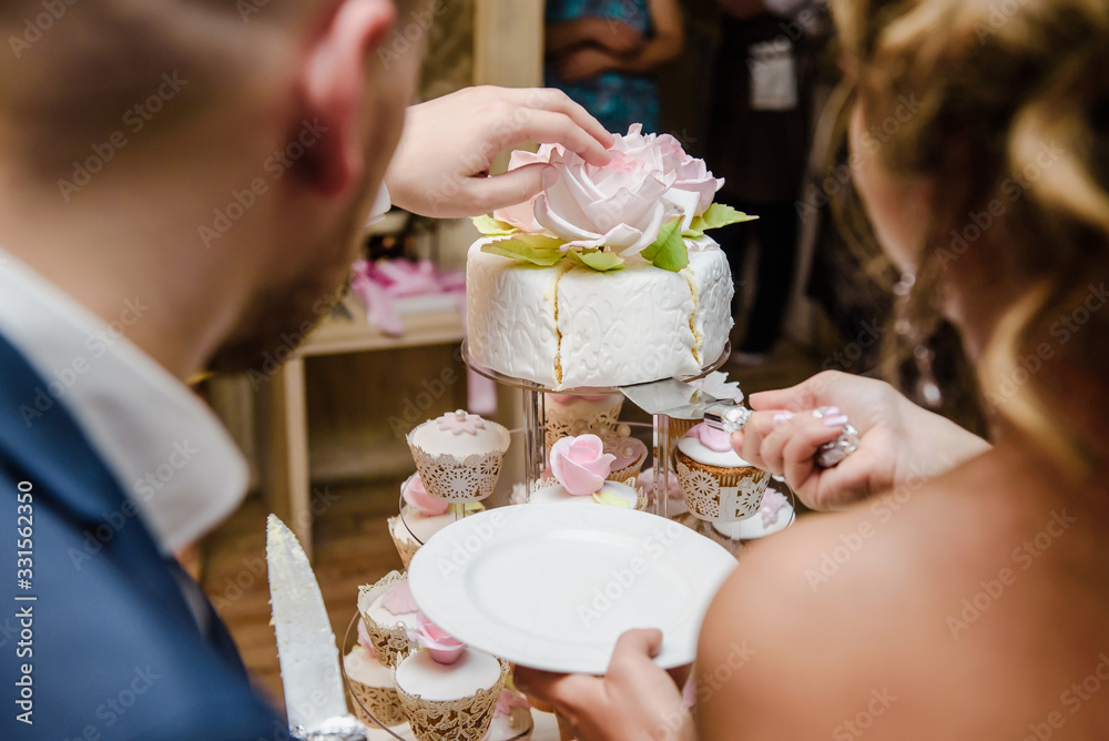 Bride and a groom is cutting their rustic wedding cake on wedding banquet. Hands cut the cake with delicate pink flowers. Bride and a groom is cutting their rustic wedding cake on wedding banquet. Hands cut the cake with delicate pink flowers.
