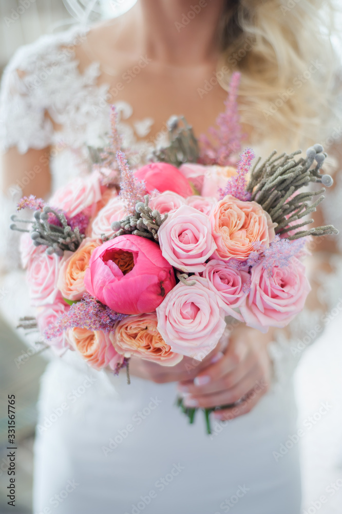 Naklejka premium White, beige, pink flowers. Bride holding bouquet. Close-up and selective focus. Beautiful bouquet of roses, peonies with ribbons in the hands of the bride, wedding details