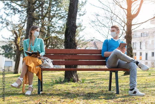 Woman and man in social distancing sitting on bench