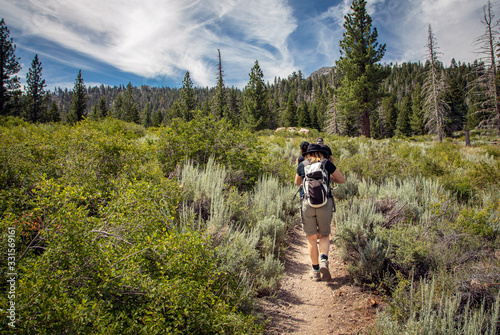 Female hiker on dirt trail in forest located in mountains. The image is horizontal and wdie angle. photo