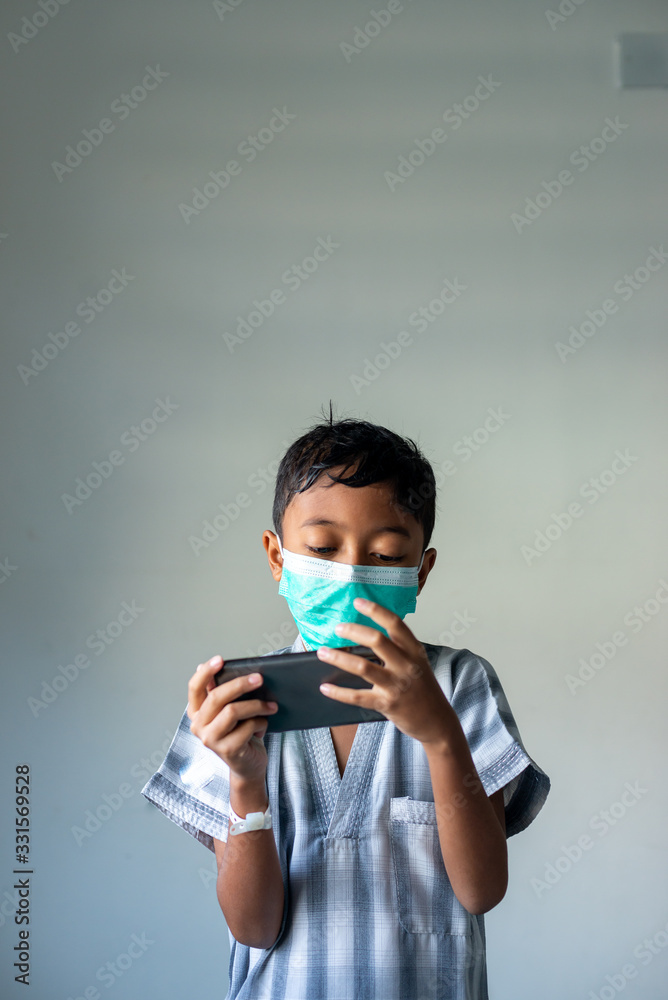 Young Muslim Boy wearing a mask playing games on the smartphone. Covid-19 coronavirus concept. Shallow depth of field. Young Muslim Boy wearing a mask playing games on the smartphone. Covid-19 coronavirus concept. Shallow depth of field.