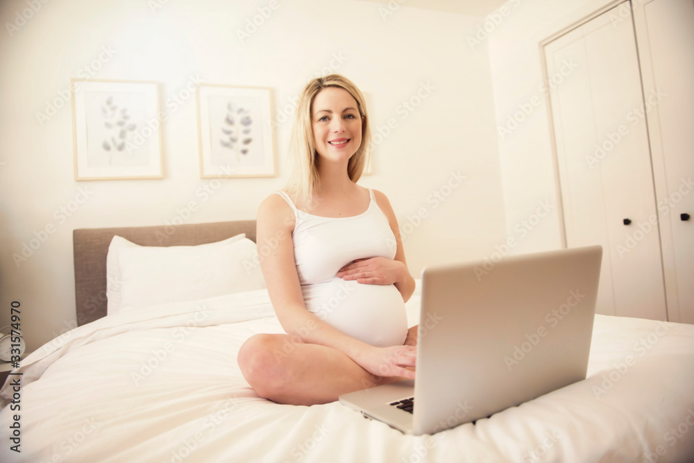 Attractive young pregnant woman with laptop on bed Attractive young pregnant woman with laptop on bed