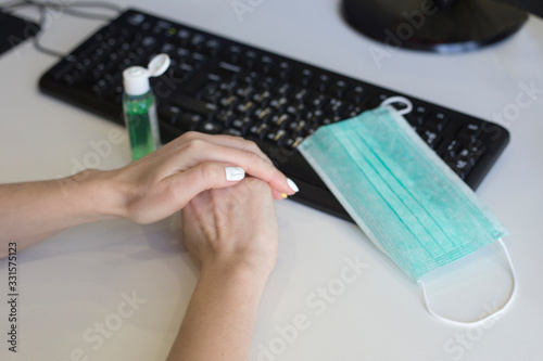 Woman disinfects hands at the workspace in the office. Hand disinfection against viruses and germs