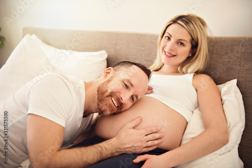Beautiful pregnant woman and her handsome husband spending time together in bed ear belly