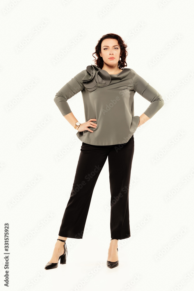 Fototapeta premium A serious woman in a gray blouse holds her hands on her belt, isolated on white background.