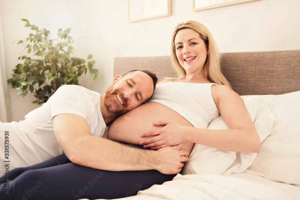 Beautiful pregnant woman and her handsome husband spending time together in bed Beautiful pregnant woman and her handsome husband spending time together in bed