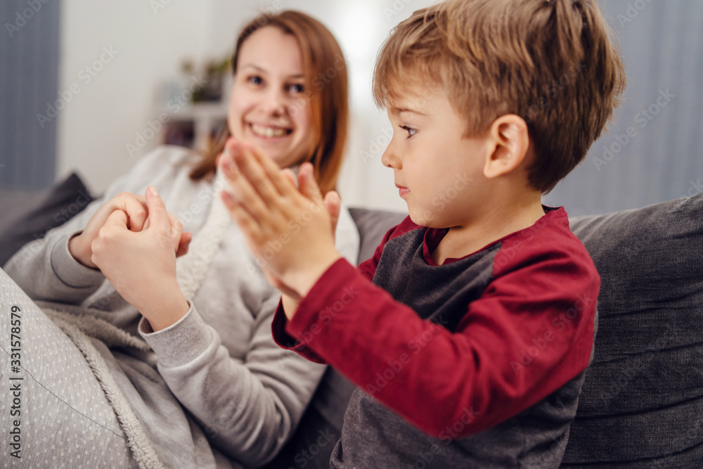 Portrait of small caucasian boy male child kid sitting on the sofa bed at home by mother young woman rubbing hands with alcohol disinfectant antibacterial prevention hygiene product prevent disease Portrait of small caucasian boy male child kid sitting on the sofa bed at home by mother young woman rubbing hands with alcohol disinfectant antibacterial prevention hygiene product prevent disease