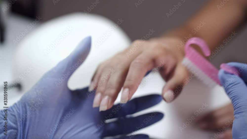 Nail artist wears blue gloves. Master holds brush for cleaning nails. Women are in beauty salon. Nail artist wears blue gloves. Master holds brush for cleaning nails. Women are in beauty salon.