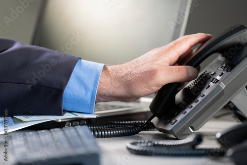 Male hand picking up telephone at an office
