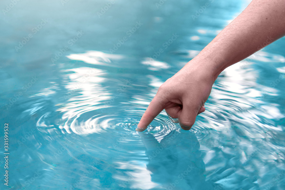 Man’s hand touching blue swimming pool water with finger.