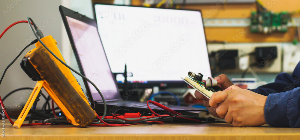 profesional technician measuring the small electronics device with digital multimeter, with blurry computer monitor in background, concept of modern repair shop. profesional technician measuring the small electronics device with digital multimeter, with blurry computer monitor in background, concept of modern repair shop.