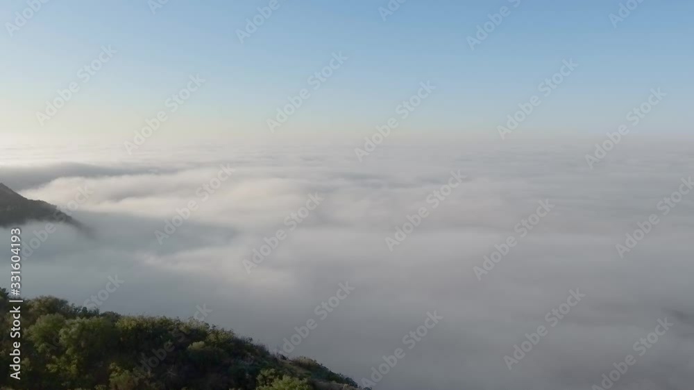 The drone camera moves from the cliff of the canyon into endless thick clouds and a mysterious foggy horizon (Malibu Canyon, Monte Nido, California, USA)