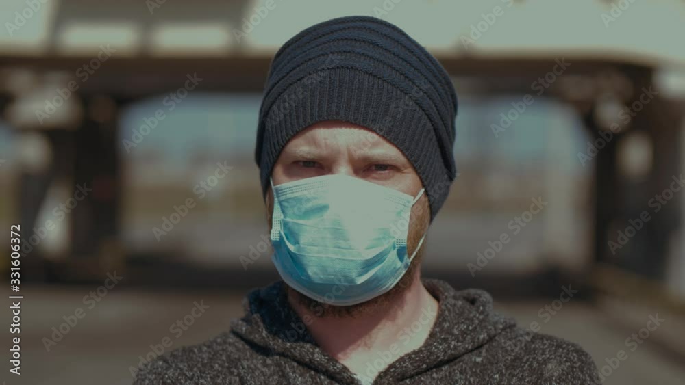 A Portrait Of Man Standing Outdoor In A Medical Mask For Protection Against Flu Or Coronavirus Looking To The Camera . Corona Virus Pandemic. 2019-nCoV. COVID-19. Slow Motions. 4K Video A Portrait Of Man Standing Outdoor In A Medical Mask For Protection Against Flu Or Coronavirus Looking To The Camera . Corona Virus Pandemic. 2019-nCoV. COVID-19. Slow Motions. 4K Video