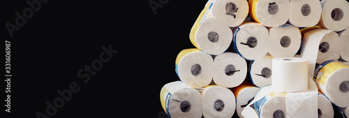 A large stack of white paper rolls packages. Header for webseite, banner, horizontal poster with dark background. World wide toilet paper crisis related to the outbreak of the COVID-19 coronavirus.