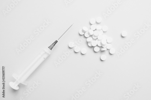 .many white pills and syringe on a light background
