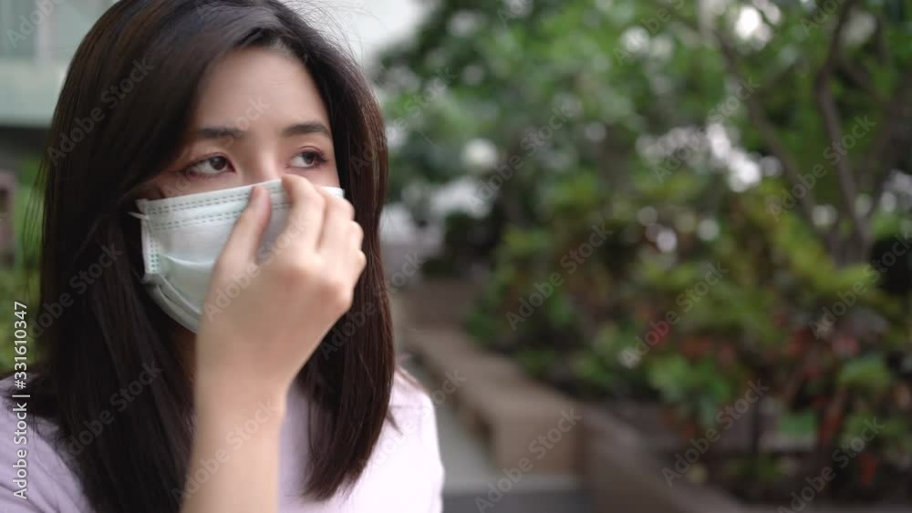 4k Asian working woman put on white protective mask waling by green bushes blurred background, health and medical concept, virus illness sickness prevention, stay at home,social distance rules, curfew 4k Asian working woman put on white protective mask waling by green bushes blurred background, health and medical concept, virus illness sickness prevention, stay at home,social distance rules, curfew