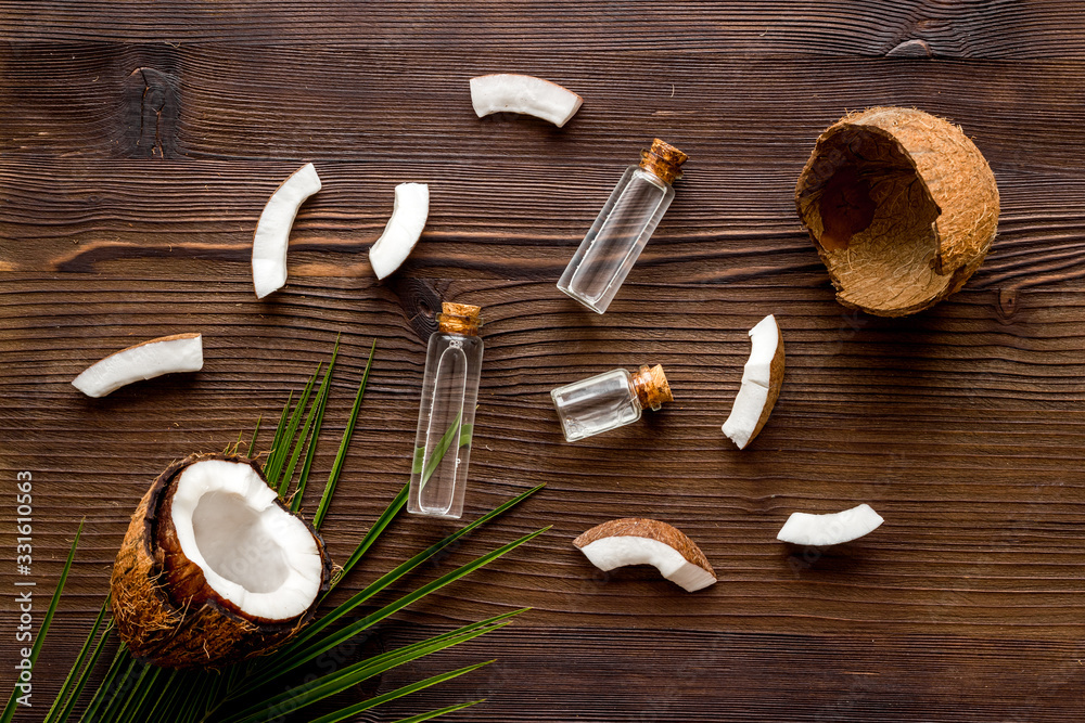 Coconut cosmetics. Organic oil in small bottles on dark wooden background top-down Coconut cosmetics. Organic oil in small bottles on dark wooden background top-down