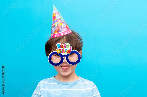 Funny grimaces of a boy in big glasses and a festive hat. Children's holiday concept