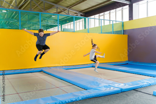 Happy smiling small kids jumping on indoors trampoline in entertainment center