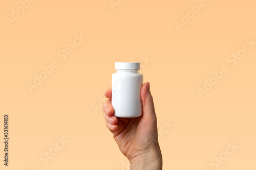Viral disease prevention concept. Female hand holds jar with vitamins, pills, medicines or drugs on orange background. Coronavirus prevention. Safety rules during quarantine. Copy space for text