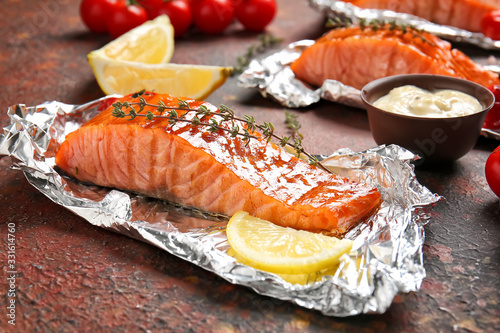 Foil with cooked salmon fillet on color background photo