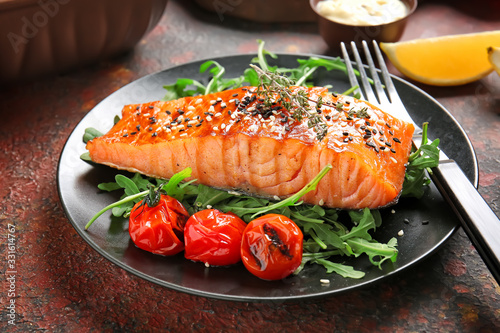 Plate with cooked salmon fillet on color background