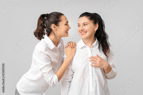 Portrait of adult daughter and her mother on grey background