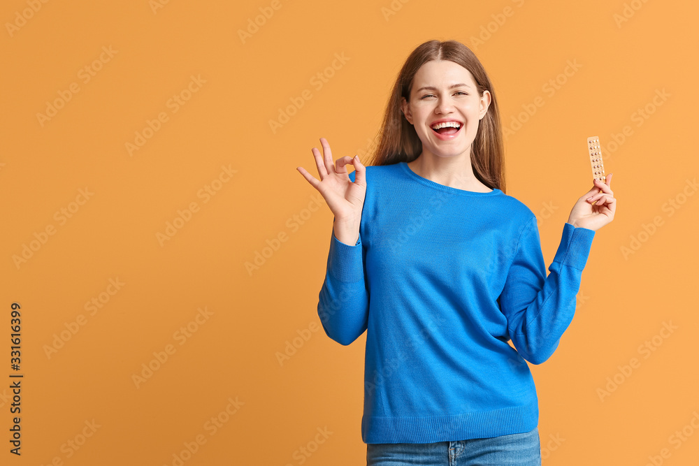Young woman with birth control pills showing OK on color background Young woman with birth control pills showing OK on color background