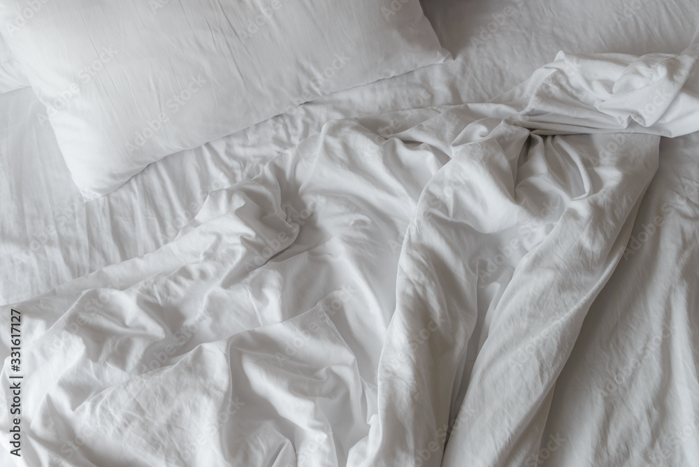 wrinkled white blanket with soft pillows on comfortable bed in the morning. messed up after nights sleep
