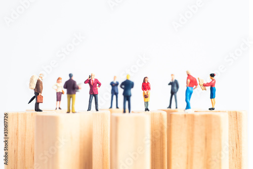 Side view of miniature toys standing on wooden block - social distancing, anti-social or team work concept.