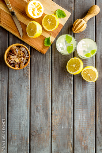 Homemade lemonade in glasses near juicer and cut lemons on wooden background top-down copy space