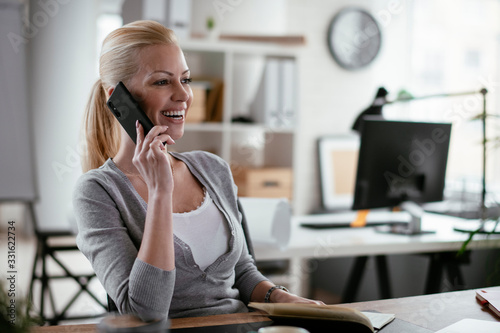 Businesswoman using phone. Happy young woman talking on smartphone in office. 