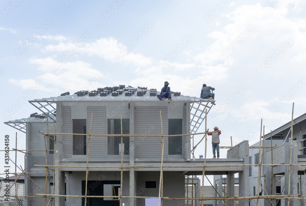 Housing property construction progress, people are building a precast house, the workman working on the roof in a hot day under cloudy sky Housing property construction progress, people are building a precast house, the workman working on the roof in a hot day under cloudy sky
