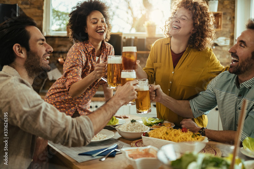 Group of happy friends having fun while toasting with beer at dining table. photo