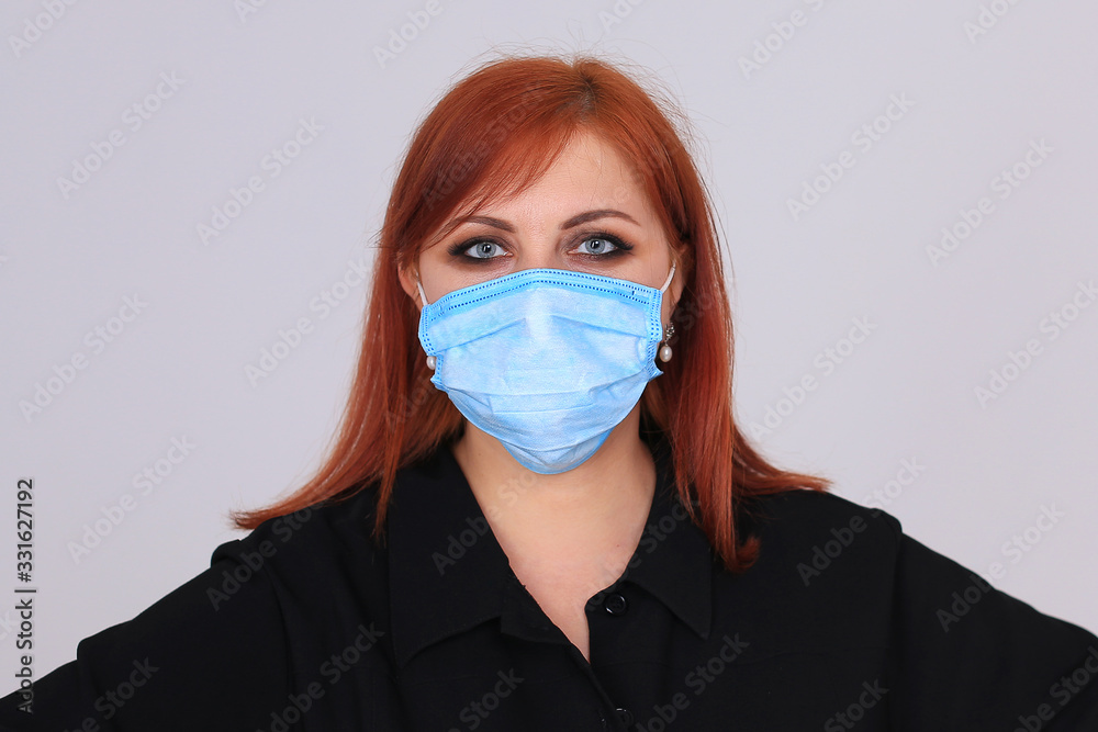 Portrait of a red-haired girl in black in a blue medical mask on a gray background Portrait of a red-haired girl in black in a blue medical mask on a gray background