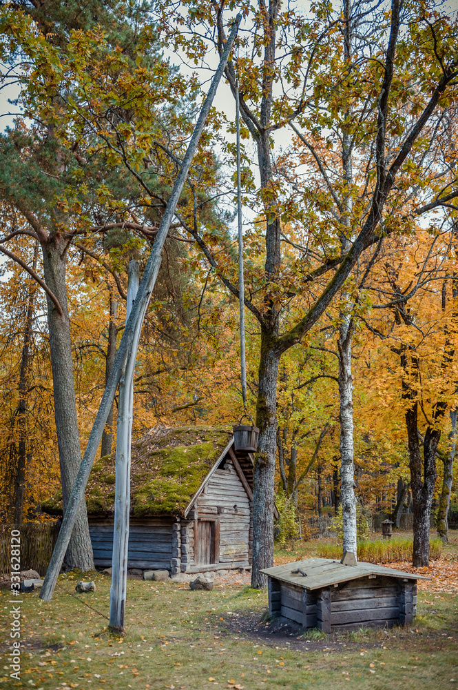 Old draw-well (shadoof) over cattle-shed and autumn nature background. Wooden buildings in the Open air museum of Latvia. Baltic Old draw-well (shadoof) over cattle-shed and autumn nature background. Wooden buildings in the Open air museum of Latvia. Baltic