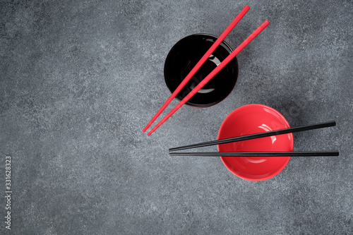 Two empty black and red rice bowls with red and black bamboo chopsticks on gray concrete background with copy space
