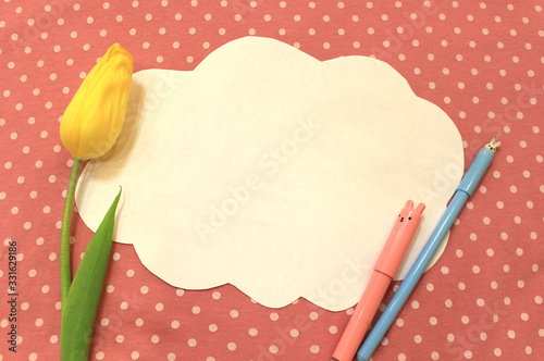 Photo of white paper in the shape of cloud on pink polka dot fabric. Background for text, greetings, invitations, holiday, Easter. Color abstract mockup template with pen pencil marker flower tulip
