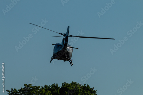 A black helicopter flies away over tree tops