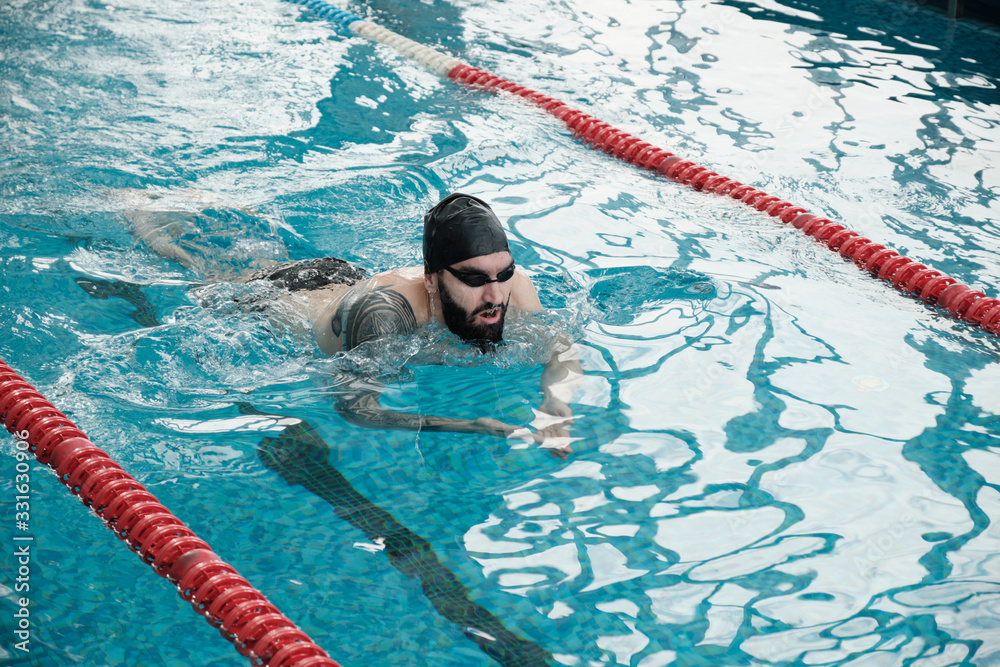 Bearded man in goggles and cap swimming brass while crossing swimming pool