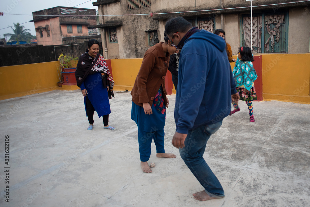 A cheerful Indian Bengali family in winter garments enjoying in a sunny winter afternoon by playing football on a rooftop. Indian lifestyle.