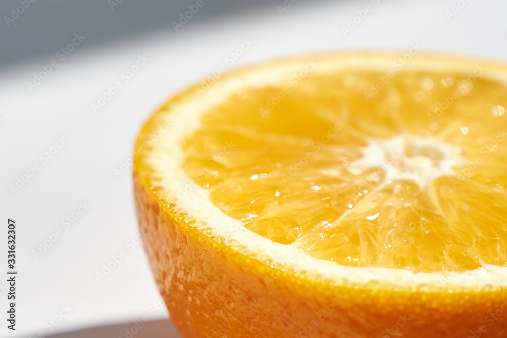 Half of ripe orange on white wooden background, close-up shot from the side in harsh sunlight.