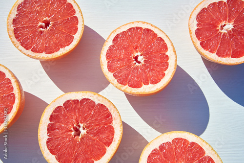 Ripe grapefruit halves on white wooden background, close-up shot from above in harsh sunlight with long colored shadows.